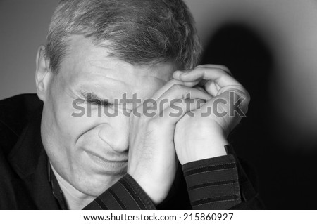 Grey-haired man in a suit at the age of forty-six years old hands covers one eye on the background of a rough wall with texture