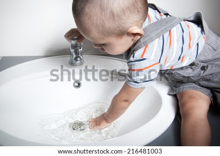 Adorable  little boy at the age of two in a striped T-shirt  looking at the flow of water in the sink