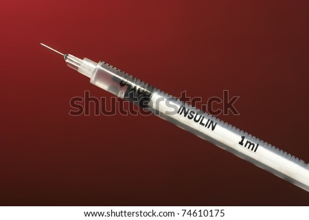 closeup view of small white insulin syringe with medicine on dark red background