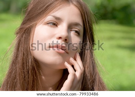 portrait of young woman with clear skin is touching her face by hand in park on green background