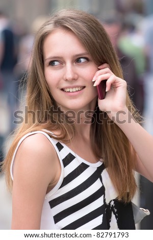 portrait of cute girl is talking via mobile phone on the street and smiling