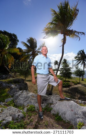Stock image of a senior old man posing in a nature setting with his leg on a rock