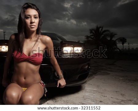 Beautiful woman in a bikini posing by a car