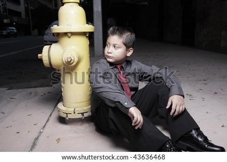 Young boy in business clothing sitting by a fire hydrant