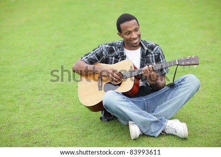 Happy black man playing guitar in the park