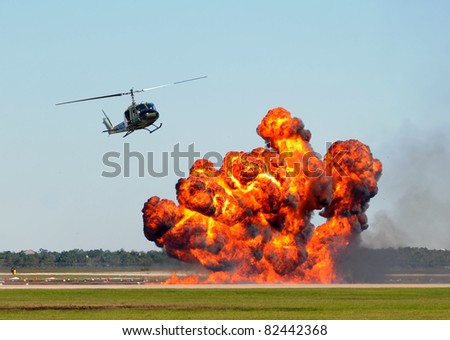 Helicopter hoving over giant ground explosion and fire