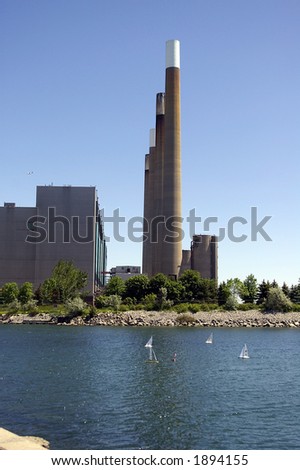 Four waterfront smoke stacks at a coal-powered electric generating station.  Model sailboats visible in water in front of stacks.