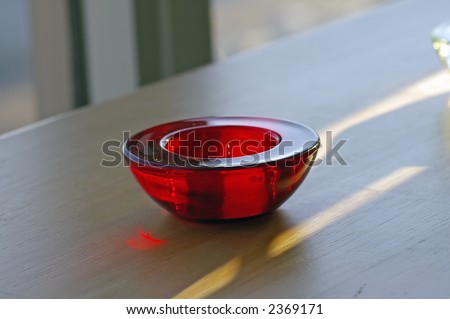 Closeup of a red glass tealight candle holder on a butcher-bock tabletop.  Visible light, shadow, and reflections.