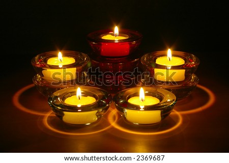 Five (5) tealight candles in glass holders arranged in three levels at night.