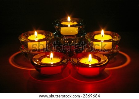Five (5) tealight candles in glass holders arranged in three levels at night.