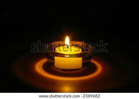 Single tealight candle in a glass holder at night.