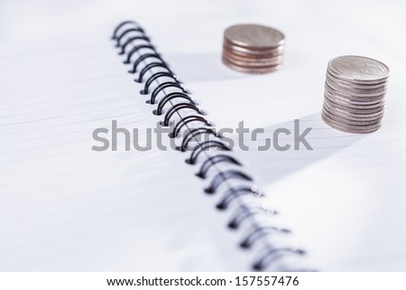 Stack of coins on empty notebook on isolated white background