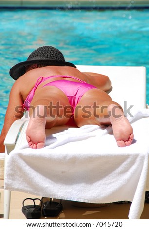 Woman sun tanning by the swimming pool in bright sun light