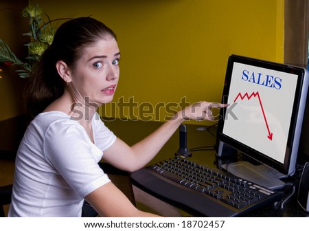 Lovely brunette female at her office workstation showing a bad economy