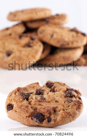 Close up of a chocolate chip cookie with a pile of chocolate chip cookies unsharp in the background on white
