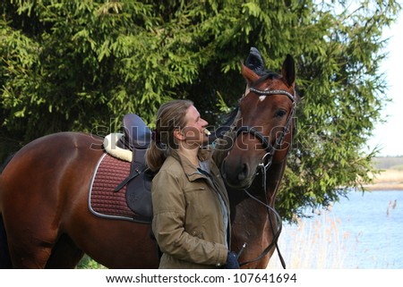 Portrait of young blonde woman and beautiful brown horse in the forest in the spring