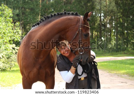 Happy smiling elderly woman and brown horse portrait in the forest