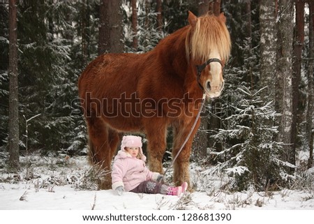 Small adorable girl sitting in the snow in forest and big palomino horse standing near