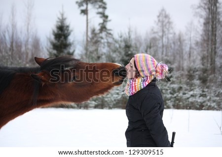 Beautiful teenager girl playfully kissing brown horse in winter forest