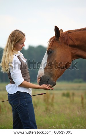 Beautiful blonde woman feeding brown horse