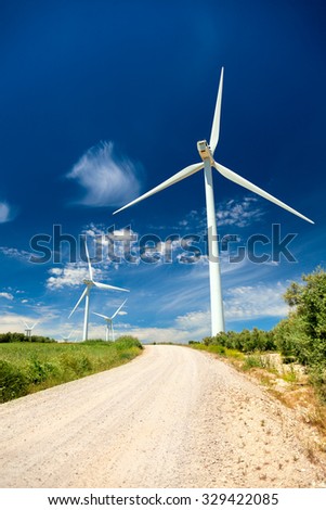 Green renewable energy concept - wind generator turbines in real landscape with grass and road, vertical