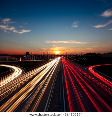 Speed Traffic light trails on motorway highway at sundown, long exposure, urban background with sun and dark sky