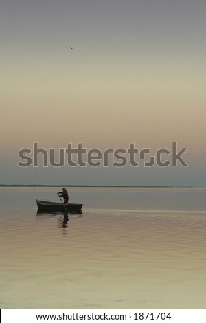 Lonely boat on silent water. Sunset. Beautiful reflection in water. One the man in a boat and one bird in the sky.
