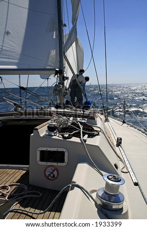 Two men work with sails.  Aboard a beautiful yacht there is a rigging, cords and blocks.