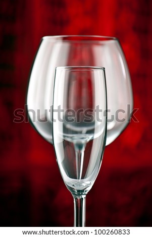 Champagne glass standing in front of a red wine glass on a table with beautiful dark red background