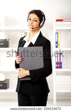 Pretty young business brunette girl with earphones on her ears smiling in her office