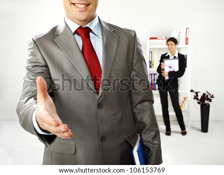 Business man and business women in the office hi is ready for a handshake while she is behind him