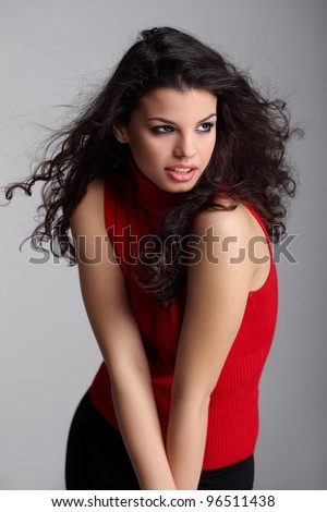 Pretty curly haired brunette girl in red turtleneck sweater and black pants posing