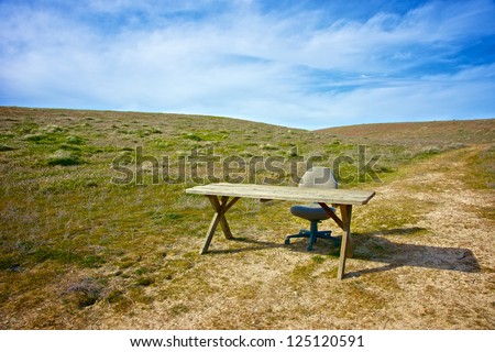 Wooden desk and office chair sit on the empty rolling plains.