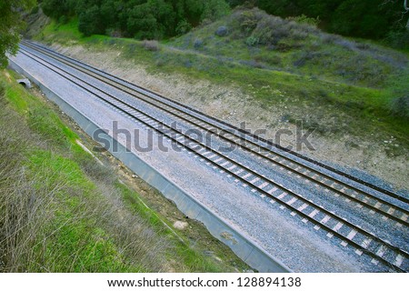 Railroad tracks run parallel to each other out of a pass between two hills.