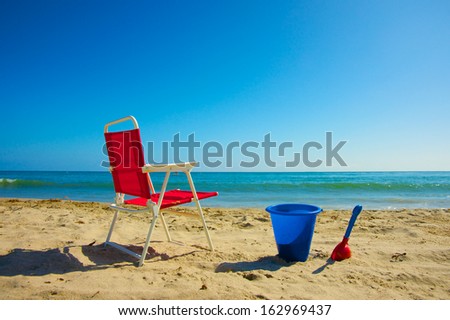 Beach chair and plastic toy buck for a child sit along a warm stretch of beach.