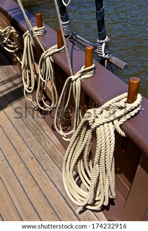 Huge bundles of rope hang alongside a wooden ship's rail.