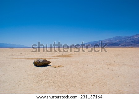 Single grey rock sits on the hard dirt of a dry lake bed in southern California\'s Mojave desert.