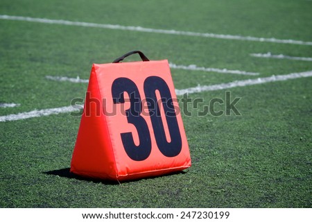 Orange yard marker designates the thirty yard line on a football field.