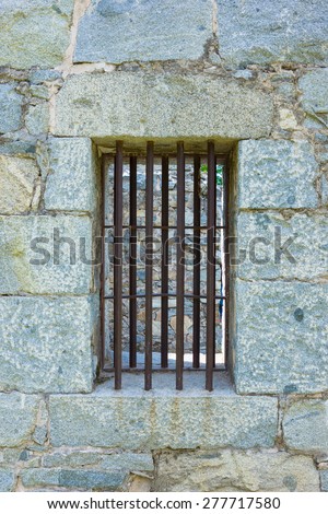 Iron bars close off the wall of an old jail cell window.
