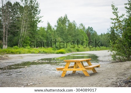 Wooden lunch table beside a calm stream in the woods and forest of Alaska.