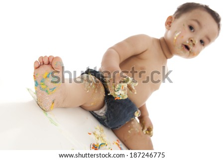 Cake smash.  Adorable baby boy covered in cake and frosting.  Focus is on foot in front.  Isolated on white with room for your text.