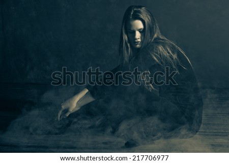 Attractive young woman in a room full of fog.  Low lighting and fog to give a moody feel to the image.  Image also includes noise for effect.