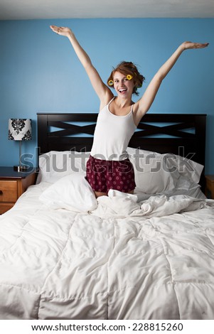 Good Morning!  Attractive teen kneeling in her bed, arms in the air and a big smile on her face.  Room for your text.