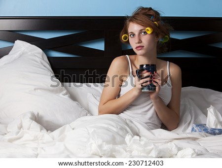 Sick Day.  Attractive teen lying in bed, holding a coffee mug, with tissues all over the bed.