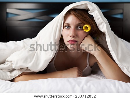 Morning.  Attractive teen with curlers in her hair and lying in her bed under the covers.