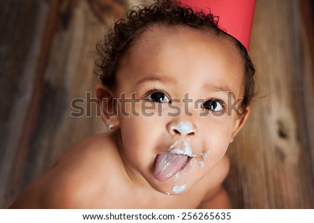 Close up of an adorable baby boy with cake icing all over his face and his tongue sticking out.