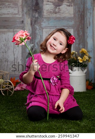 Adorable preschooler sitting in the grass and holding a fake flower.