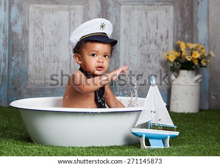 Little Sailor.  Adorable baby boy wearing a sailor hat and tie playing in the water.  Toy sailboat leaning against the wash basin.