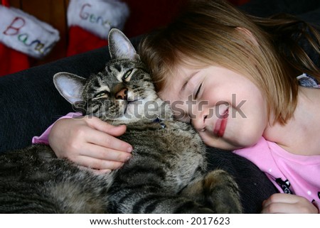 Adorable little girl snuggling with her pet cat.  Christmas stockings hanging in the background.