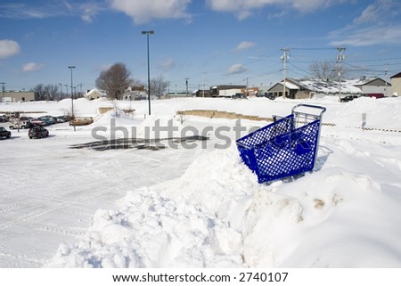 Shopping cart at the top of tall snow bank in a parking lot.